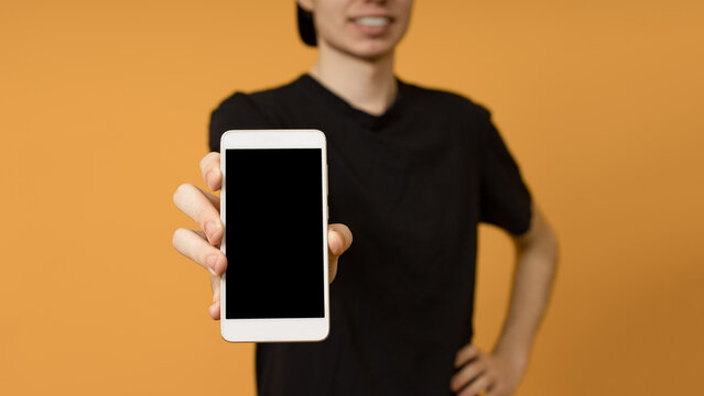 young man in a black t-shirt shows a mobile phone in his hand on a yellow background