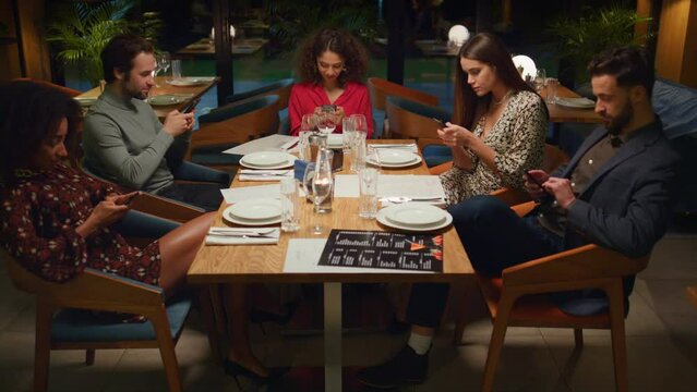 Friends table reading mobile phone browsing internet social media in restaurant.