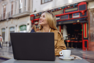 Woman sitting at table in outdoor cafe and working at laptop