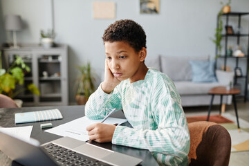 Portrait of black teenage girl looking at laptop screen while studying at home in online lesson, copy space