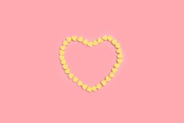 Corazones pequeños amarillos formando un figura de corazón sobre un fondo rosa pastel liso y aislado. Vista superior y de cerca. Copy space