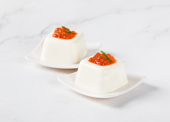 Cottage cheese cream pudding in the shape of a small square savarin, with red salmon caviar, on a serving plate. White background