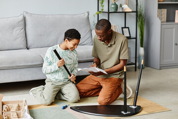 Full length portrait of African American man assembling furniture at home with daughter helping