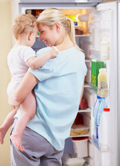 Breakfast for her baby. A mother standing in front of the fridge and holding her baby in her arms.