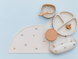 Flat lay composition with silicone baby bib and beige dishware on blue background. Flat lay, top...