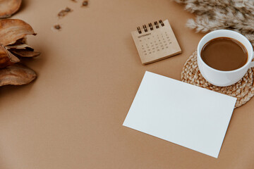 Blank paper sheet notebook, cup of coffee and calendar on beige background. Minimal aesthetic mock up