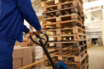 Worker moving wooden pallets with manual forklift in warehouse, closeup © New Africa