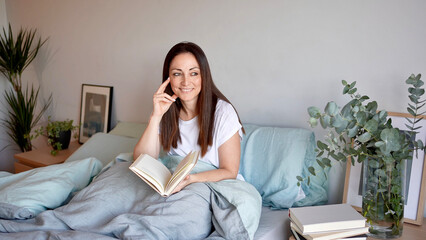 Woman looking out the window holds a book in her hands. Resting and reading in your room. Concept of love and care for yourself.