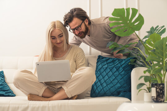 attractive cheerful married spouses sitting on a sofa, buying presents and shopping online thanks to their brand new laptop. High quality photo
