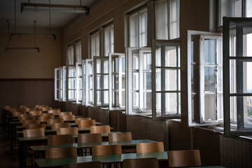 Empty old faculty or college School classroom with row of chairs, green desk tables and big white windows. Natural light.