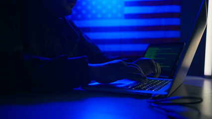 Hacker with laptop and USA flag in background. Cyber attack concept.