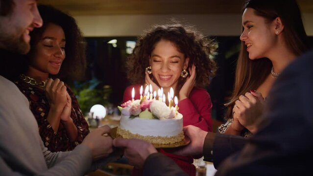 Diverse friends celebrating birthday party. Burning candles in cake surprise.
