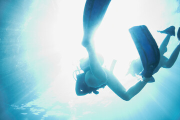 Ascending from the deep. Bottom view of two scuba divers as they ascend to the sunny surface -...