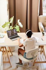 Vertical portrait of African American girl watching online lesson while studying at home in sunlight
