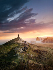 A man hiking to reach the top of a mountain summit at sunset along the UK coastline. Photo composite.