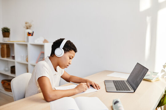 Minimal side view portrait of African American girl watching online lesson with headphones while studying at home