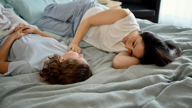 Happy mother and daughter relaxed on the bed in bedroom laugh and joke, having fun one morning on a weekend. Smiling mother supports her teenage daughter.