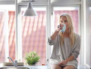 Relaxed in the morning. A pretty young woman enjoying a cup of coffee in the morning while sitting on a window sill.