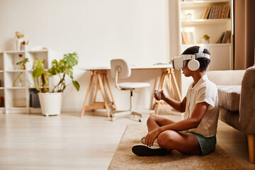 Minimal side view portrait of African American girl playing VR game while sitting on floor at home, copy space