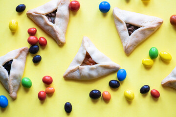 Hamantashen - traditional cookies for Jewish holiday Purim. Triangle cookies with assorted fillings on a yellow background.