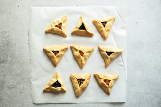 Hamantashen cookies - traditional festive baking for Purim.  Triangle cookie  with different fillings on a baking paper. Top view, gray background.