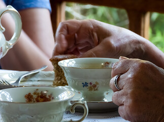 Woman hand holding tea cup. KPM porcelain tea set, decorared with flowers on a table. White lace tablecloth, silver fork.