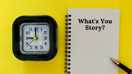 What is your story - message on white notebook. With alarm clock and yellow background. Business concept.