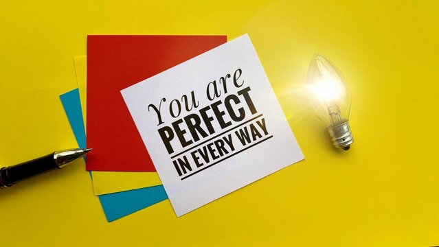 Motivational quote - You are perfect in every way. With notepads and light bulb background.