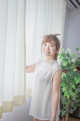 Fototapeta premium 白いカーテンから差し込む朝日を浴びる若い女性 
