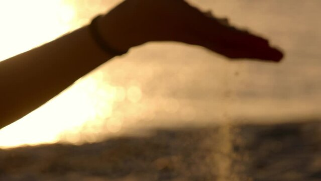 Young woman playing with sand on a beach at sunset - slow motion