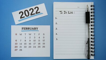 Hand written to do list text on notepad for month of February 2022. With pen and blue background....