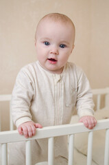 Cute little smiling infant baby girl standing in a crib in the bedroom of the home. 