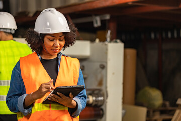 Engineer asian and african woman wearing safety helmet and vest holding clipboard and take note on...