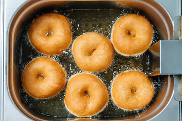 Donuts frying in deep fat. Preparation of traditional donuts, six round donuts in boiling oil.