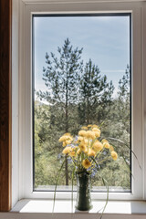 bouquet of yellow dandelions in clay vase standing on windowsill by open window in countryside