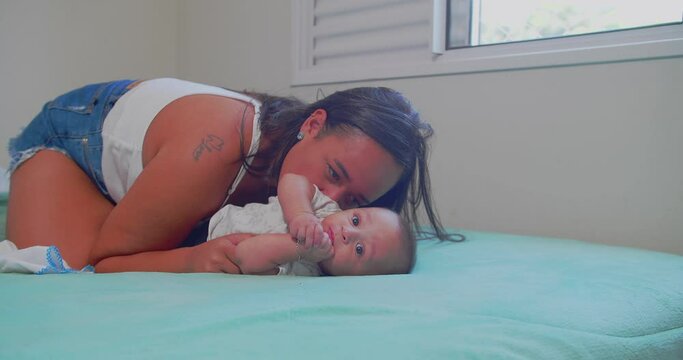a mother tickles her newborn baby on top of her bedroom bed