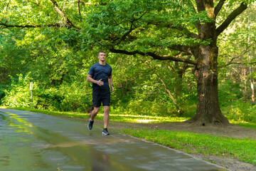 A man athlete runs in the park outdoors, around the forest, oak trees green grass young enduring athletic athlete run sport workout outdoor young jog, woods wellbeing. Summer energy feet stretches