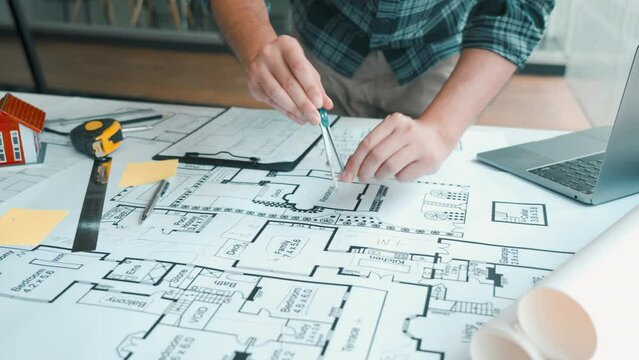 Interior designer or architect reviewing blueprints and holding pencil drawing on desk at home office.