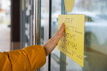 Close-up of a woman reading a braille lettering on a glass door.