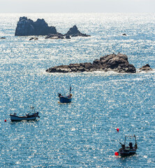Cornish fishing boats and pinnacles of rock backlit by summer sunlight, protruding from the sea...