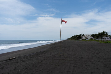 playa de arena volcánica  con fuerte viento, cono de tela roja diseñado para indicar la...