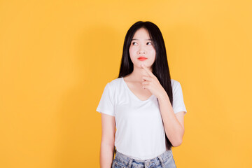 Thinking beautiful asian woman wears white t-shirt on yellow background, holding hand near the face