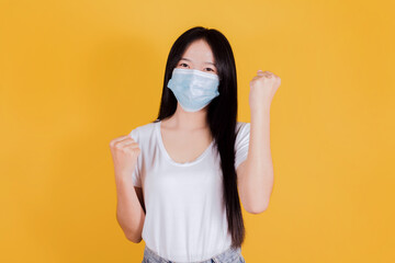 Asian woman wears white t-shirt in medical face mask to protect Covid-19 raise hands glad excited cheerful on yellow background
