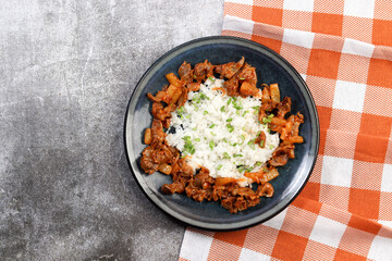 Stewed chicken gizzards with boiled rice on a round plate on a dark gray background. Top view, flat lay