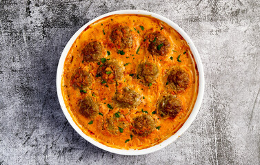 Homemade meatballs in creamy tomato sauce in a white baking dish on a dark grey background. Top view, flat lay
