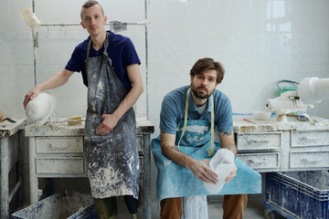 Young male staff of contemporary prosthetic factory in aprons looking at camera while making plaster casts and sockets in workshop