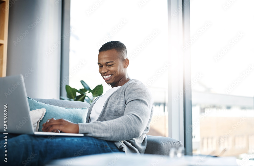 Poster his social network is joining him on the sofa. shot of a happy young man using a laptop while relaxi