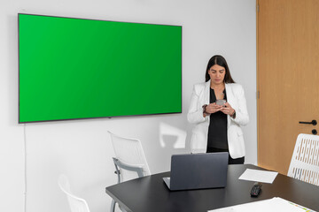 Young businesswoman texting while waiting for her presentation in the boardroom. Green screen for presentation