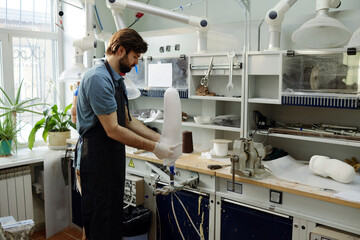 Fototapeta premium Worker of manufactory putting white sheet on workpiece of prosthetic socket to form and fix its shape by workplace