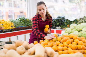 Obraz premium Focused girl who works as a salesperson in a store puts the tangerines that have fecently been put on sale on the ..counter